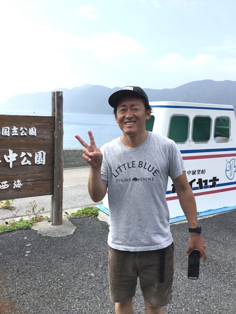 海中公園の立て看板の前で記念撮影を行う松山のダイビングショップのオーナー